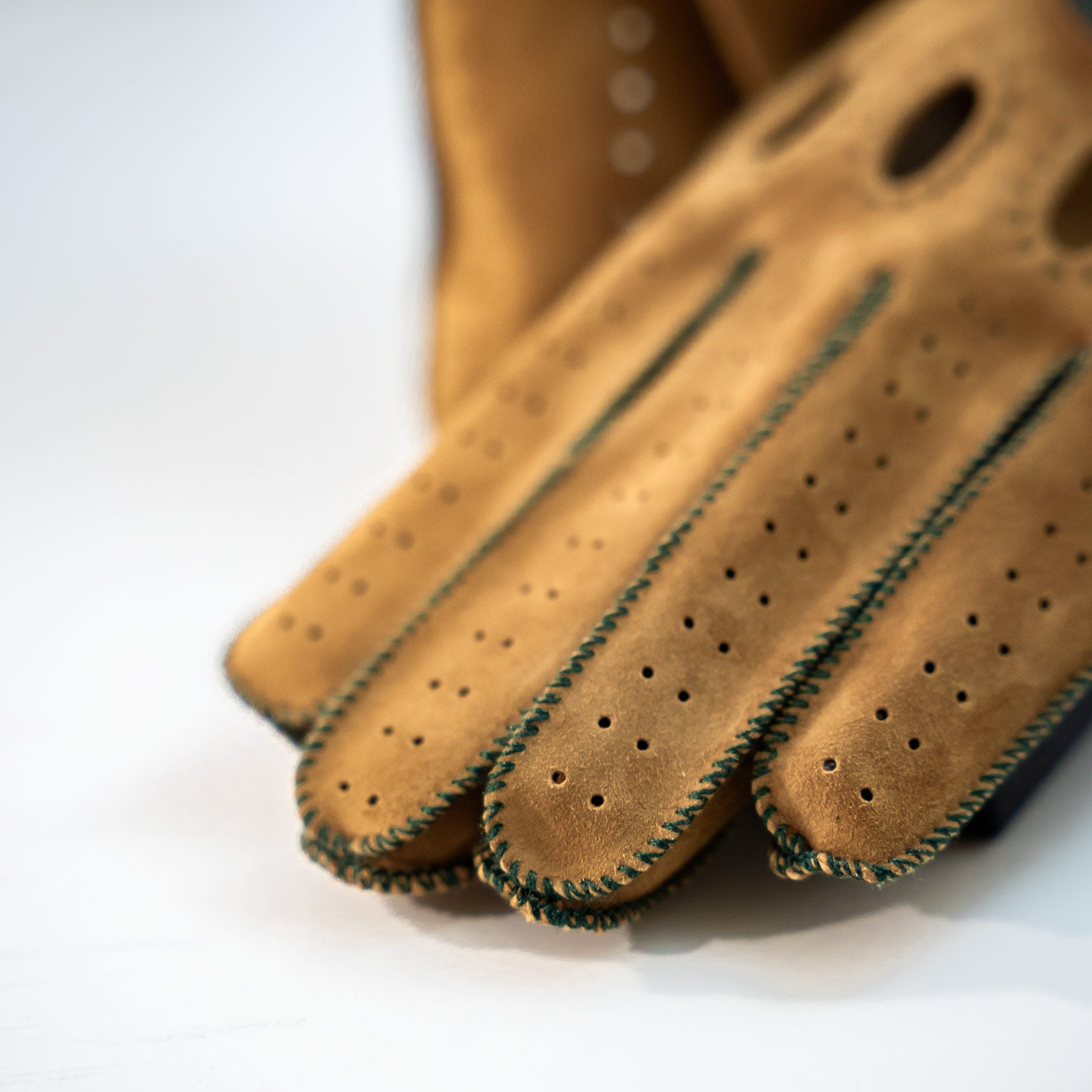 Pair of brown leather gloves with green stitching on a white background