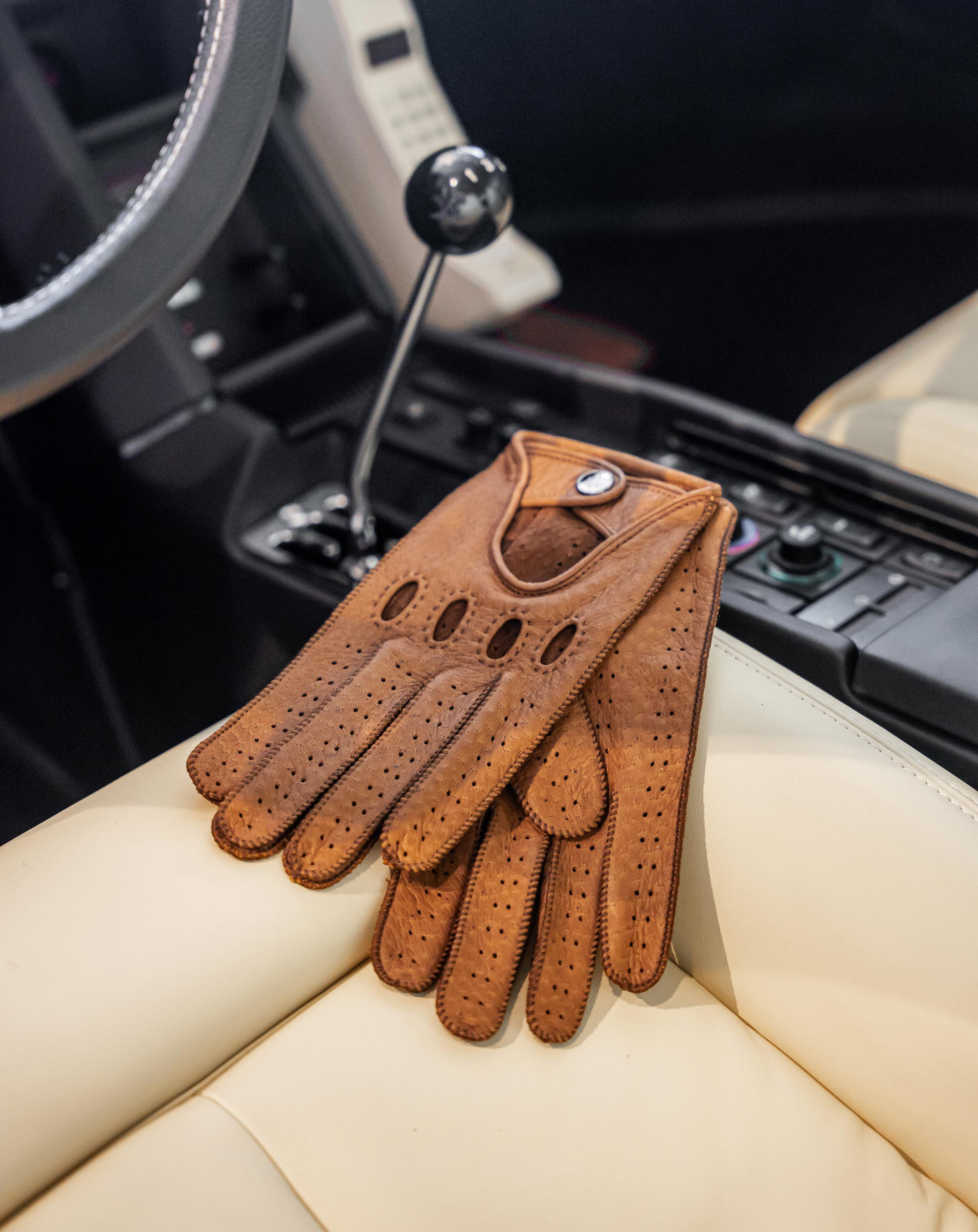 Brown leather driving glove on a car seat with gear shift and steering wheel in the background