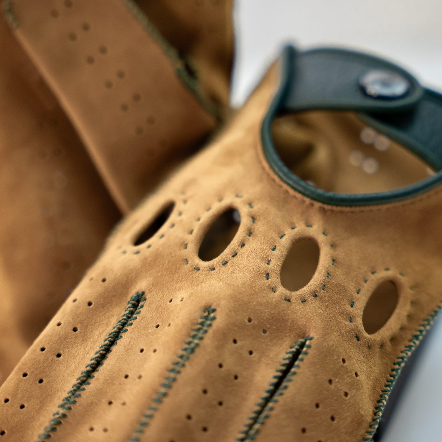 Close-up of a brown leather glove with green stitching on a white background