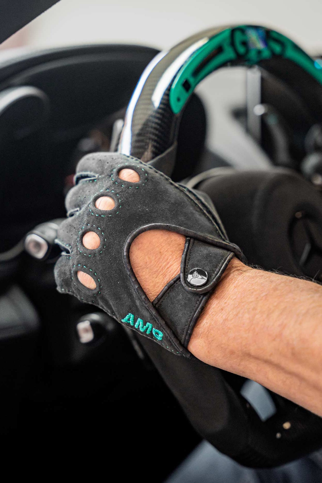 Person wearing a black driving glove with 'AMG' branding on a car steering wheel.
