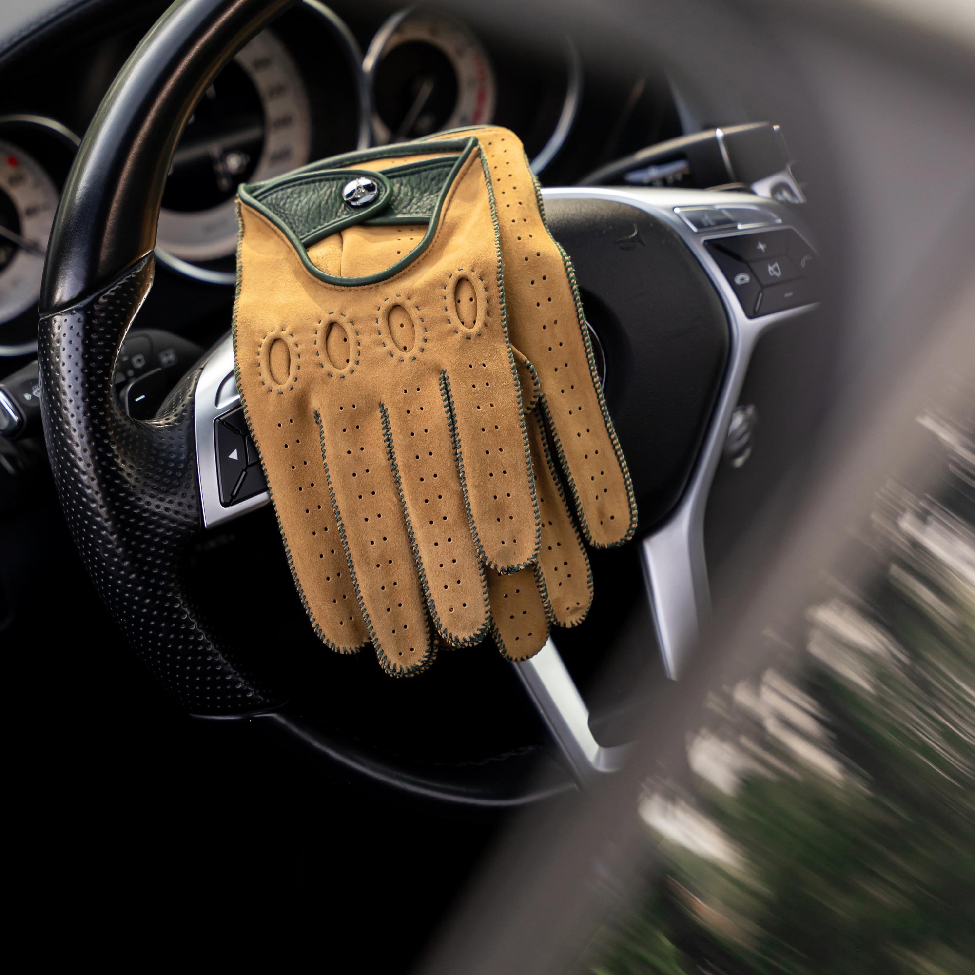 Camel suede leather Italian driving gloves, laying on a mercedes steering wheel.
