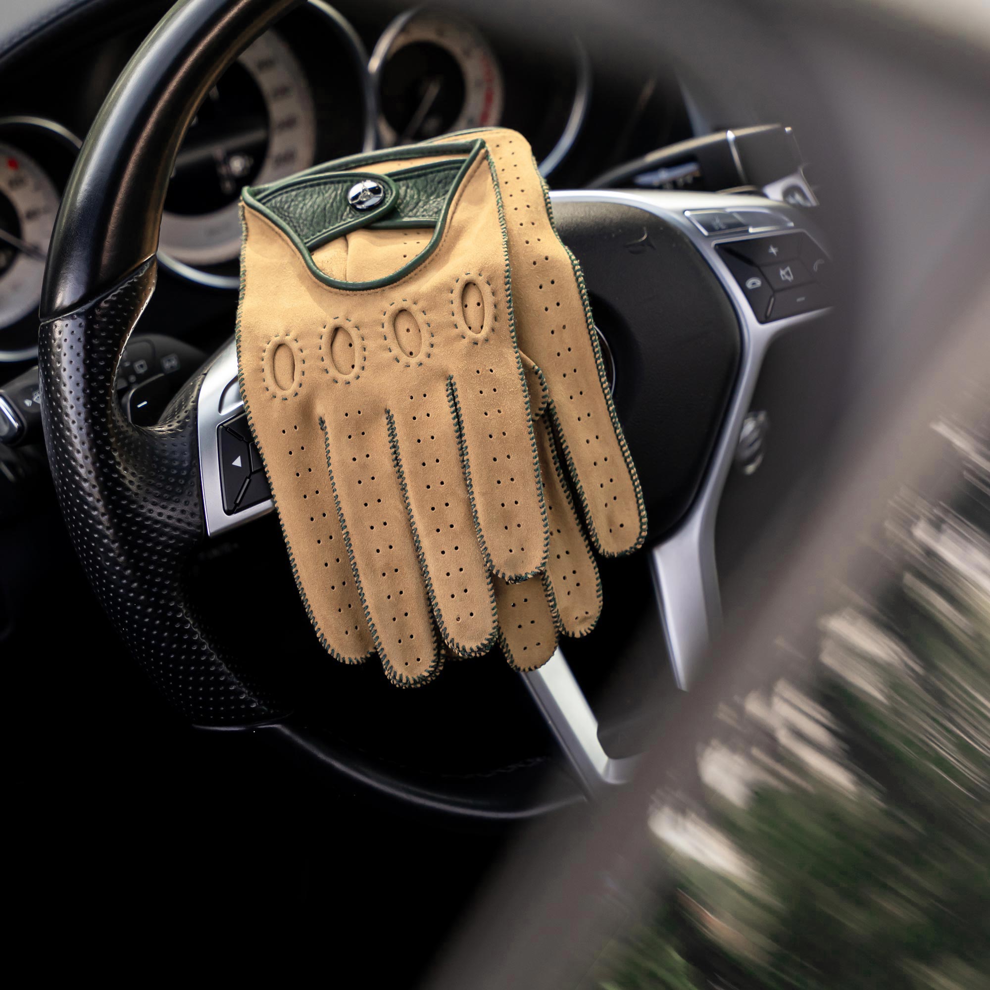 Sand with green Italian driving gloves, laying on a steering wheel of a Mercedes Benz.